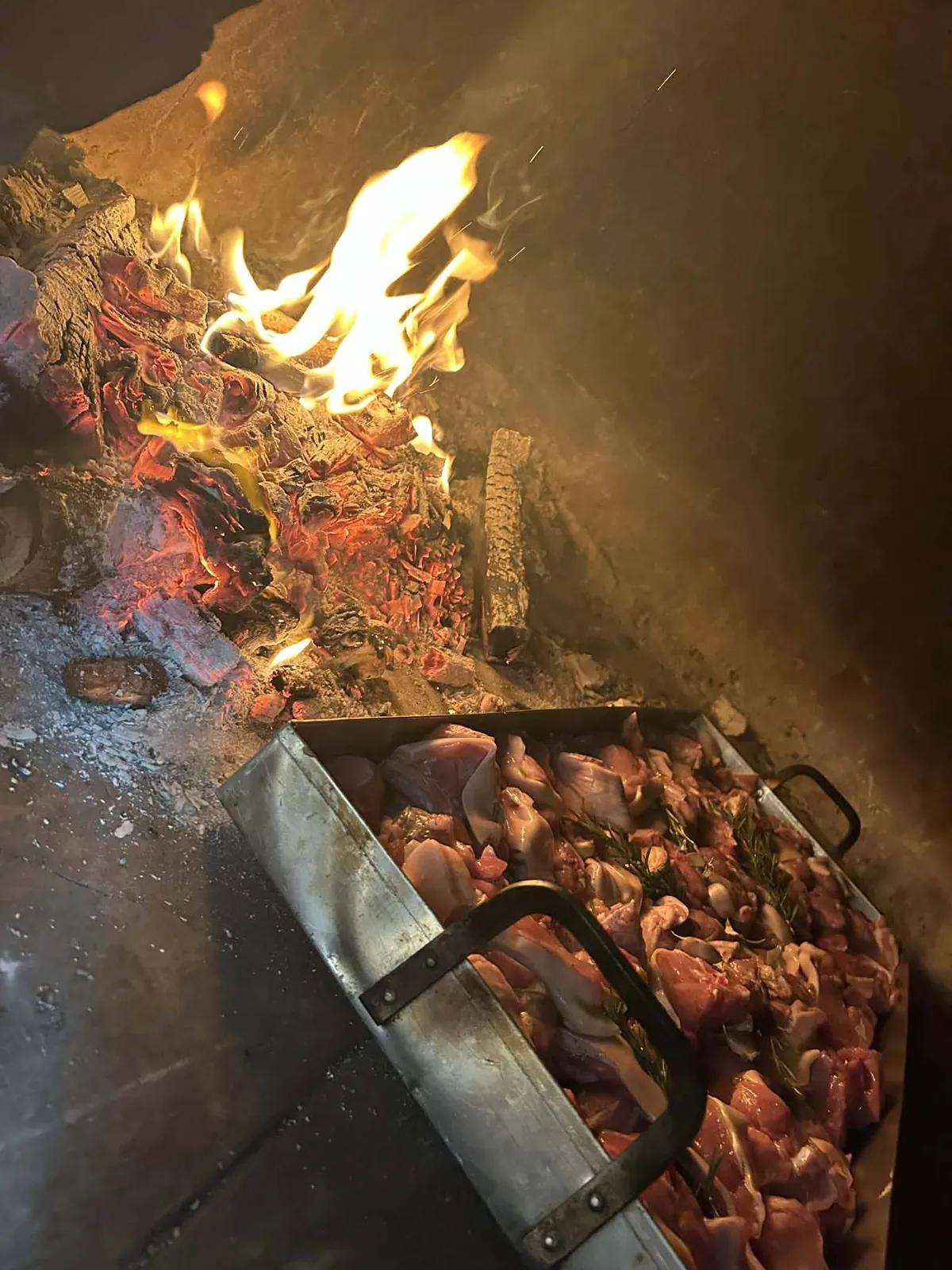 Carne che cuoce in teglia sulla brace del camino